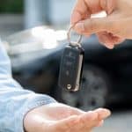 na imagem, uma pessoa entrega uma chave de carro a outra